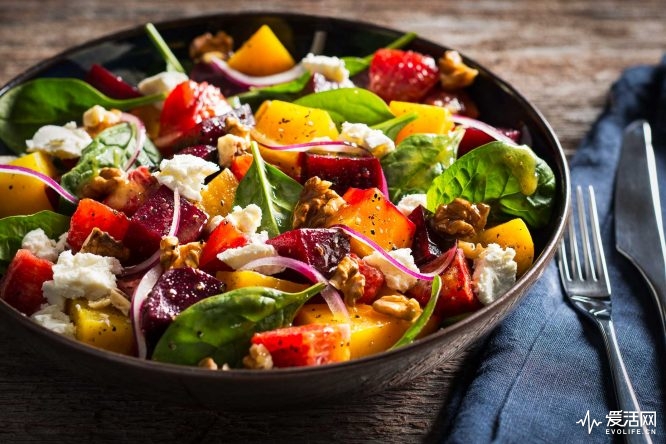 Salad of red and yellow beets, spinach, shaved red onions, blood oranges, walnuts, and goat cheese. Dressed with olive oil and black pepper in a dark glazed bowl on a rustic wood surface. For Fillipo Berio Olive Oil.